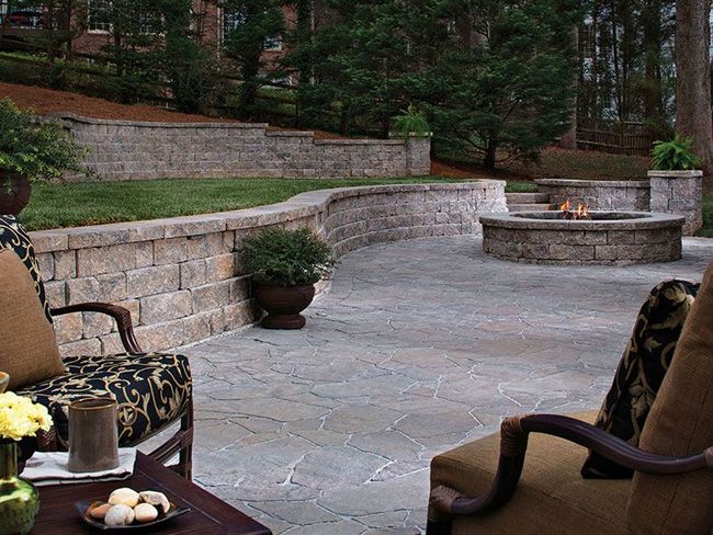 Patio with stone pavers, a circular fire pit, retaining walls, and two outdoor chairs facing the fire.