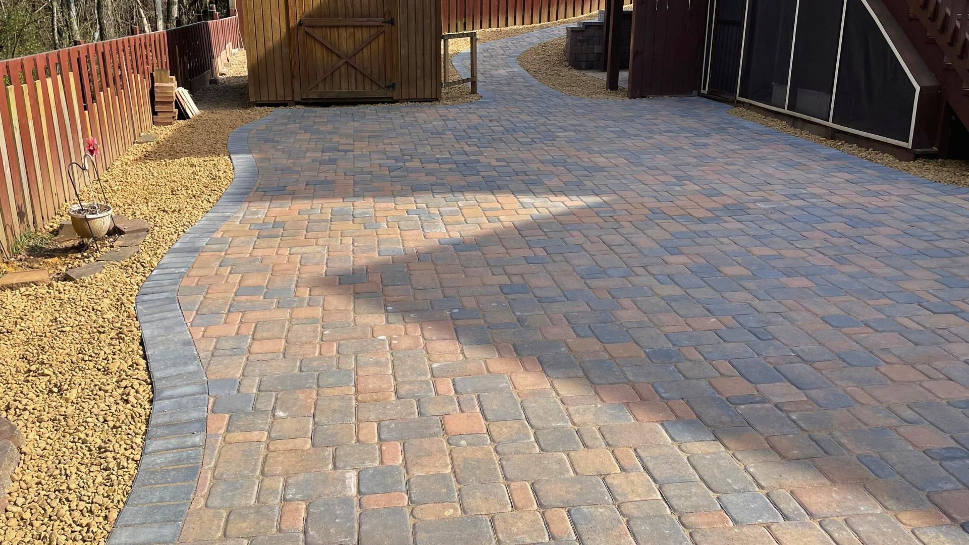 A brick driveway with a wooden fence in the background