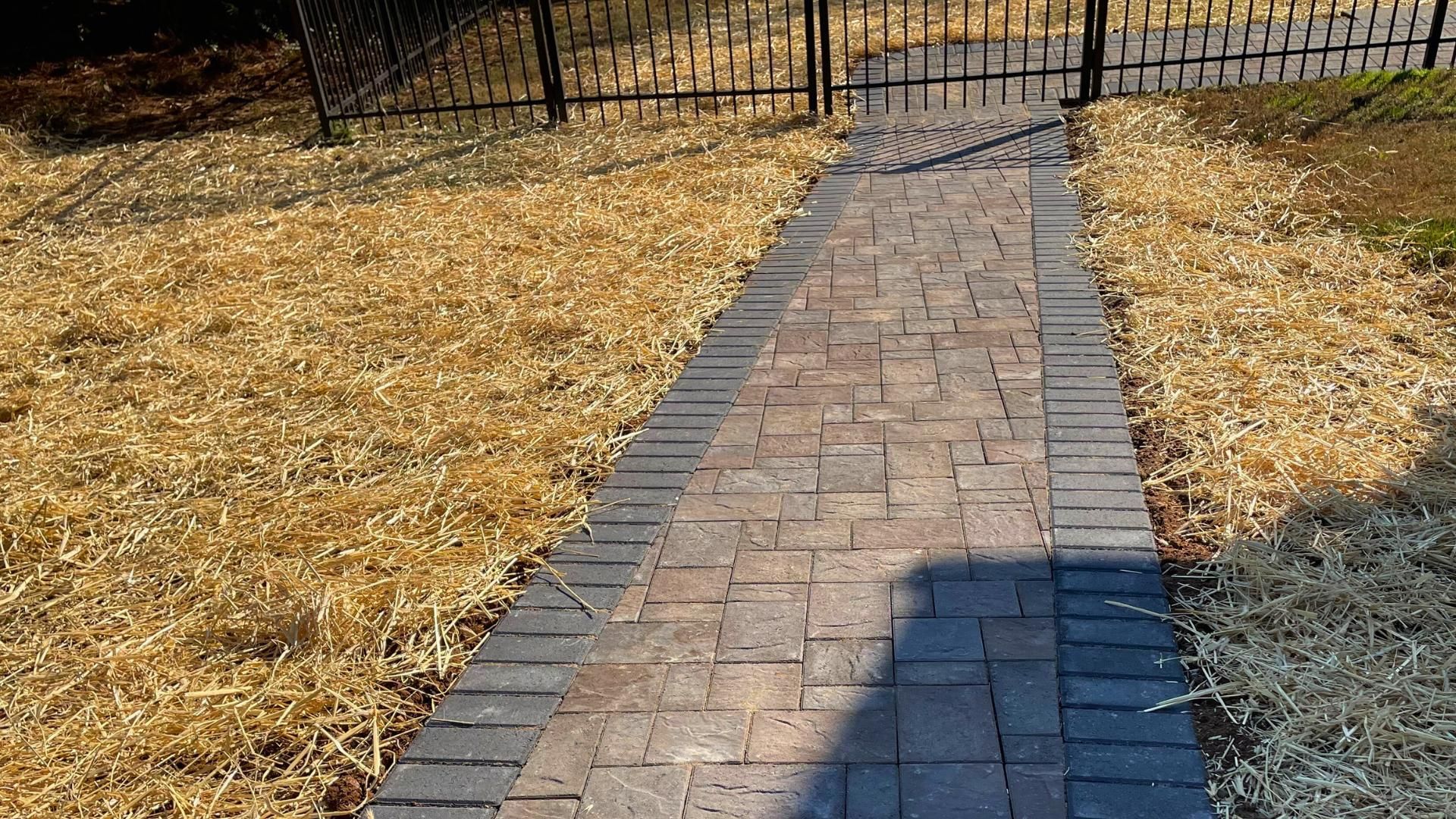 A brick walkway leading to a fence in a yard.