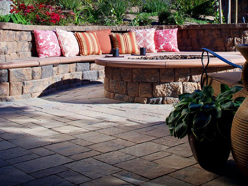 A patio with a fire pit and a bench with pillows on it