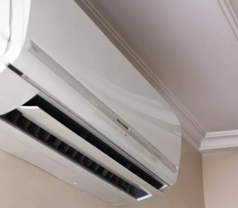A white air conditioning unit mounted on a beige wall beneath a white ceiling.