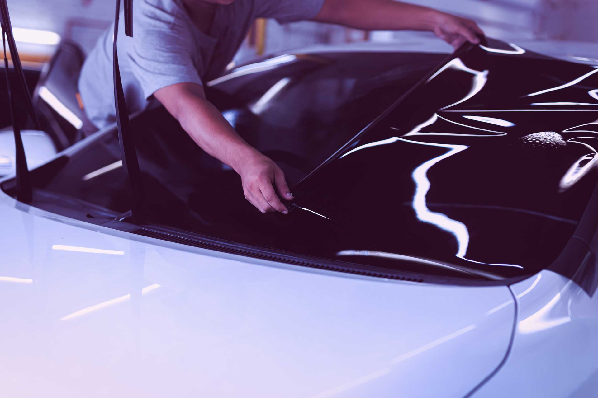 An auto shop specialist applies tinting foil to the window of a car.