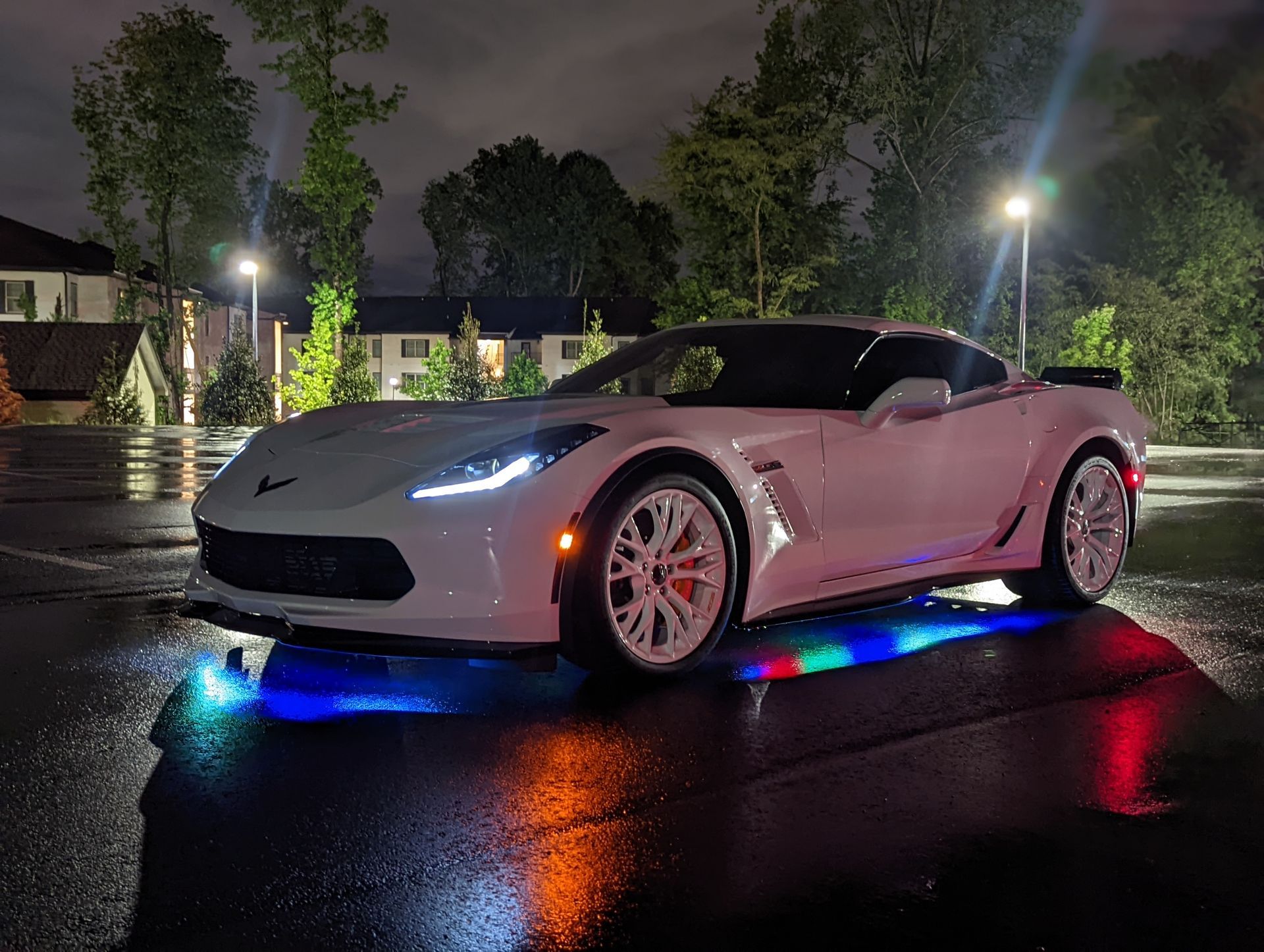 A white sports car is parked in a parking lot at night.