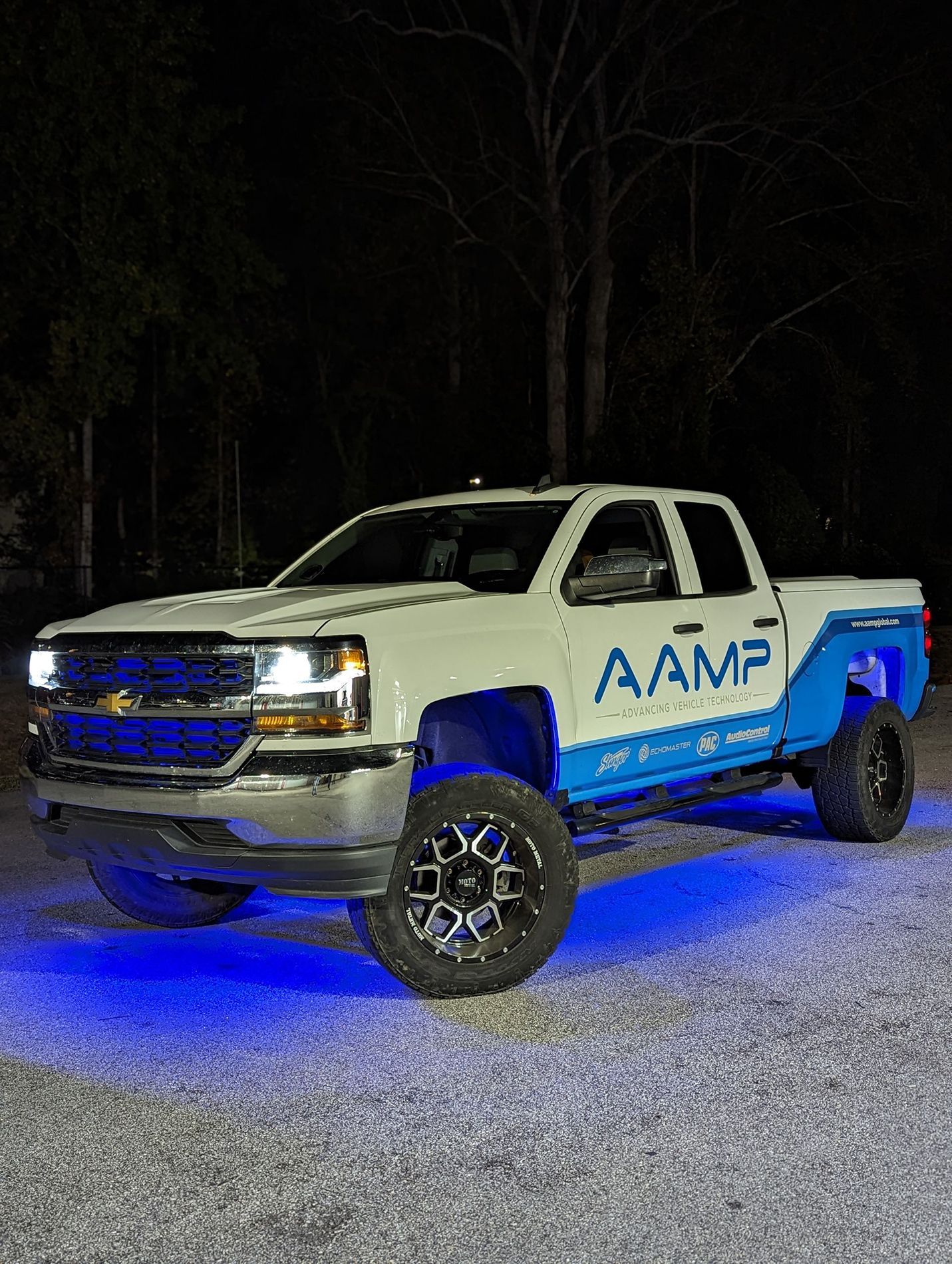 A white and blue truck is parked in a gravel lot at night.