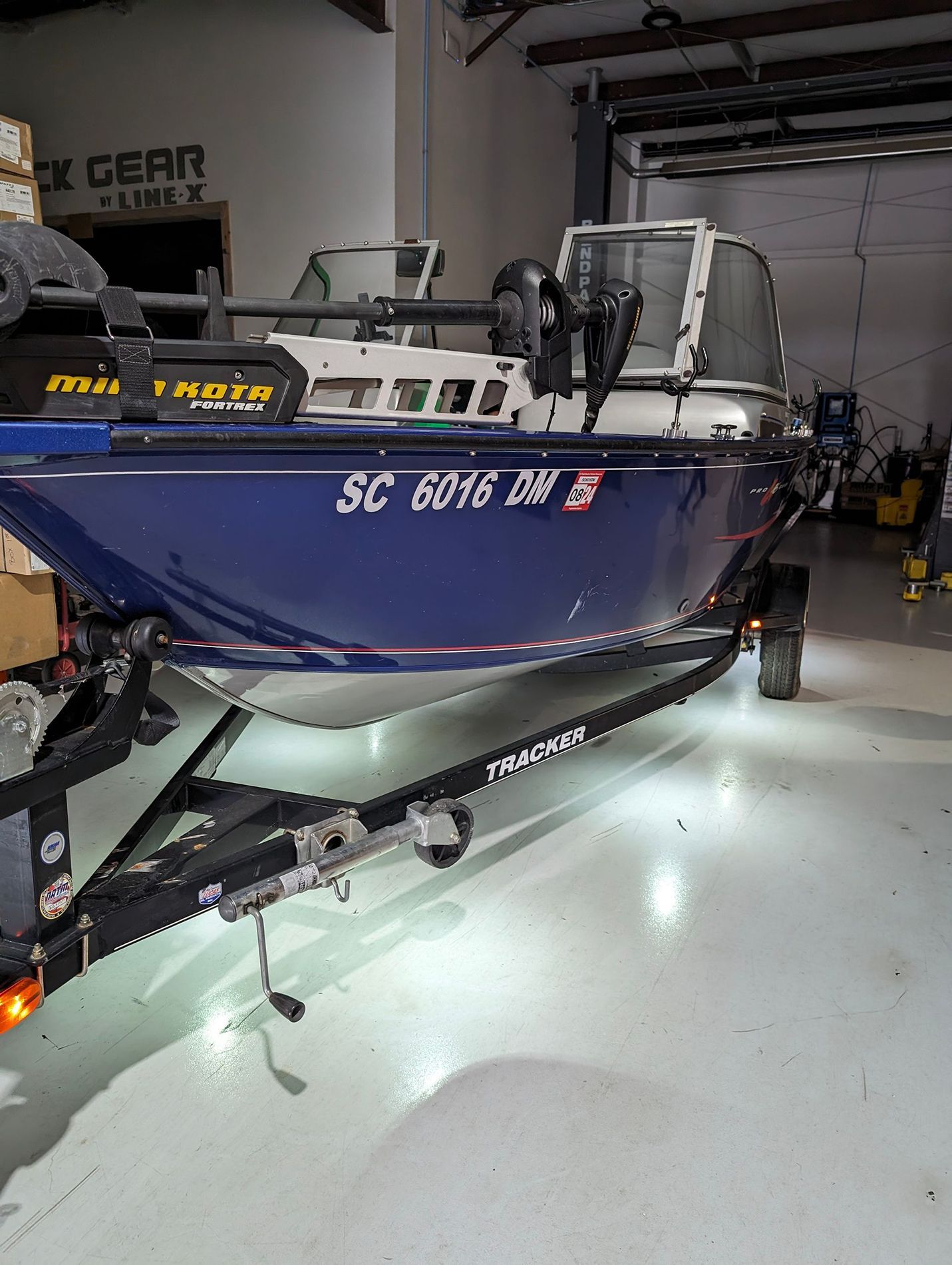 A blue fishing boat is parked on a trailer in a garage.