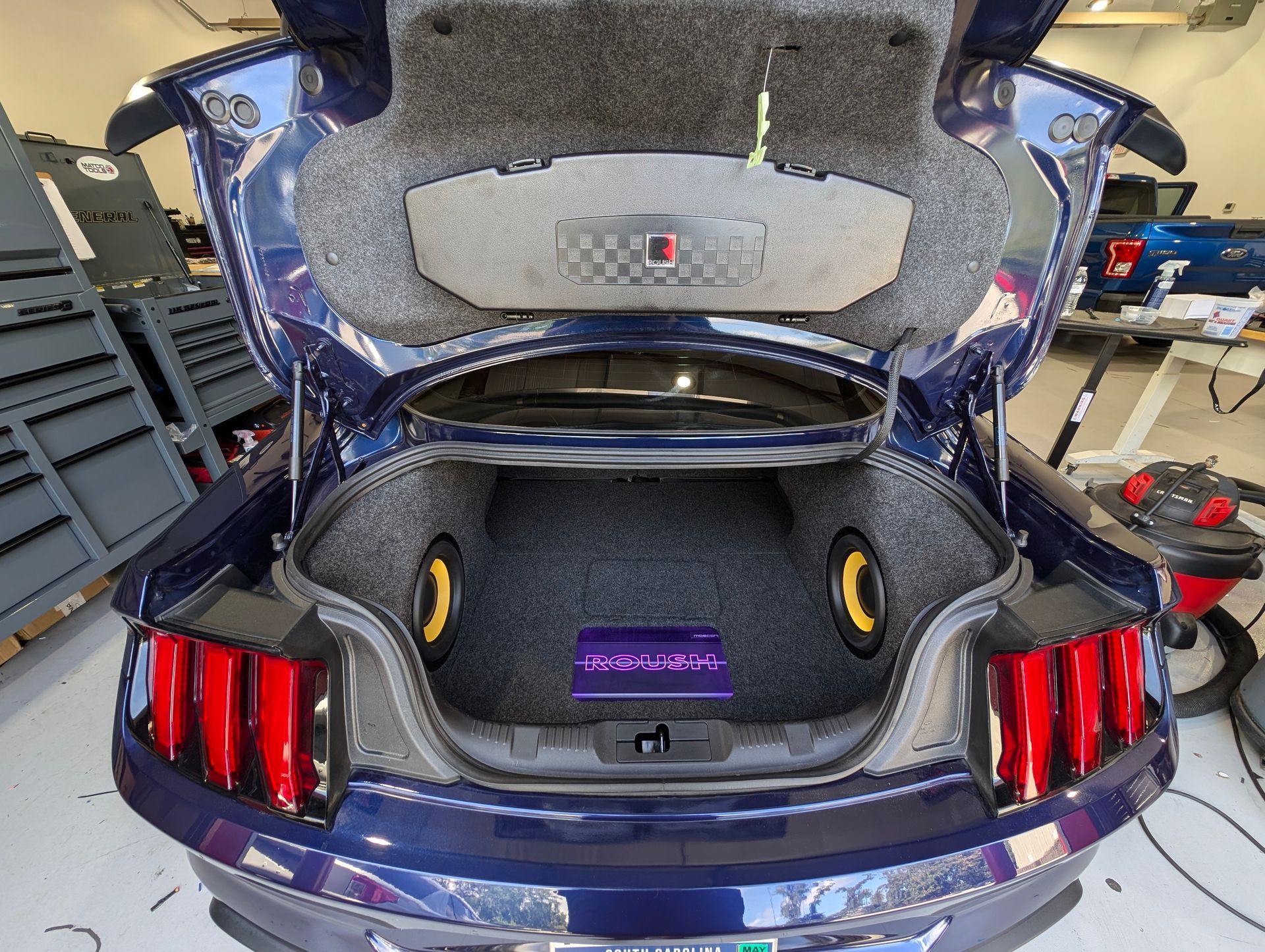 The trunk of a blue mustang with the hood open