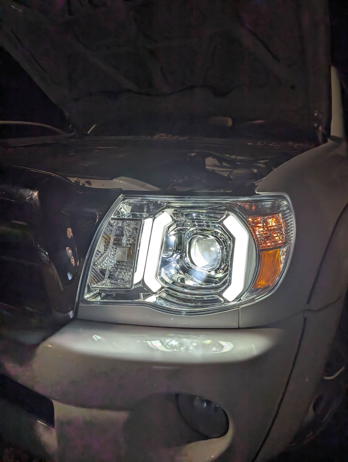 A close up of a car 's headlight with the hood open.