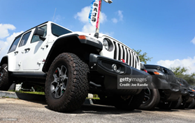 A new white Jeep with different truck accessories parked in a lot against the blue sky.