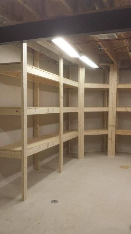Custom-built wooden storage shelving units installed against the walls of an unfinished basement with concrete floors.