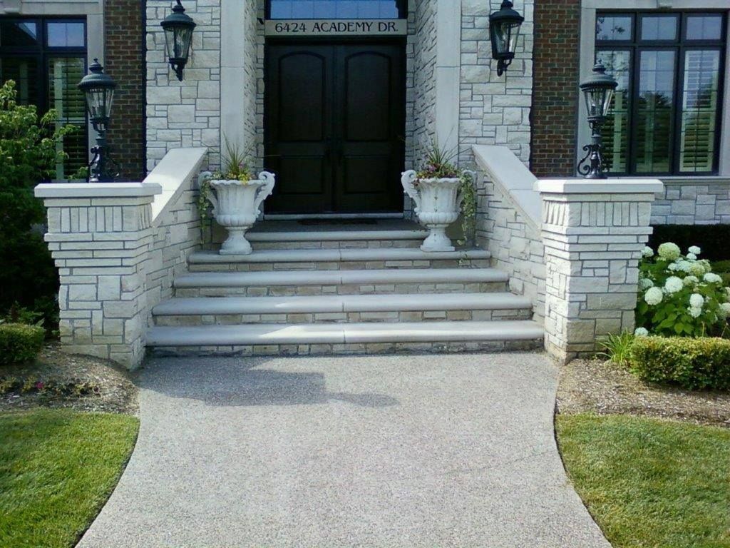 Stone stairs lead to a black double door at a home entrance, flanked by two urn planters and outdoor lanterns.