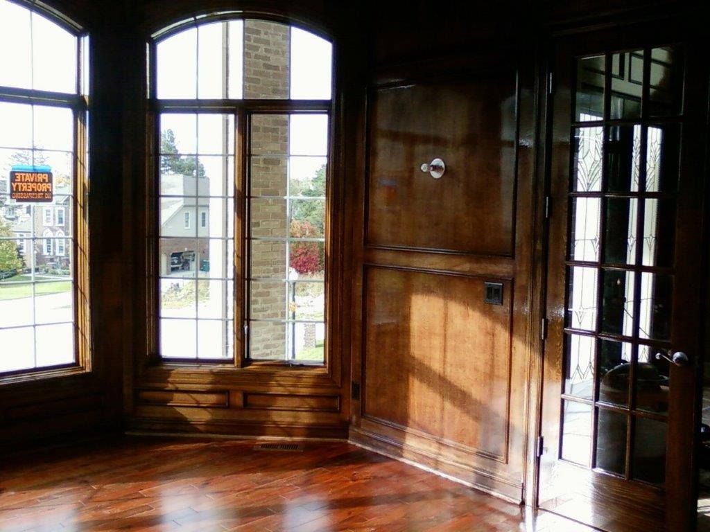 A room featuring wood-paneled walls, a polished wooden floor, large arched windows, and a glass-paneled wooden door.