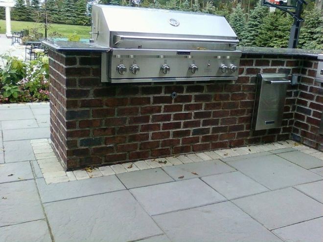 A stainless steel outdoor grill built into a red brick island on a paved patio.