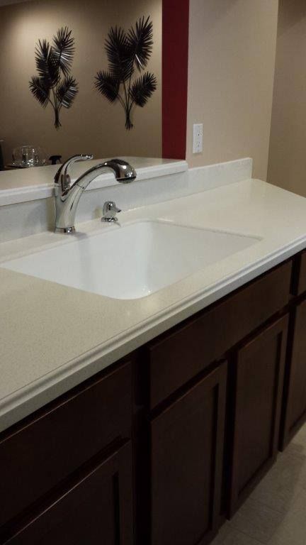 A hand uses an adjustable wrench to tighten a white plastic plumbing pipe beneath a sink.