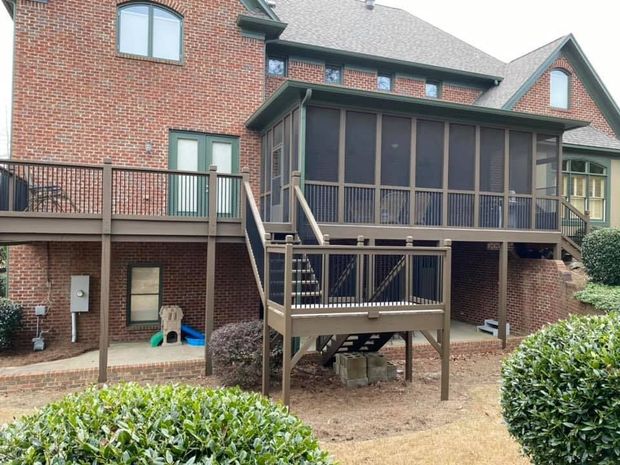 Backyard deck with screened porch, brick house. Brown deck and railing. Overcast day.