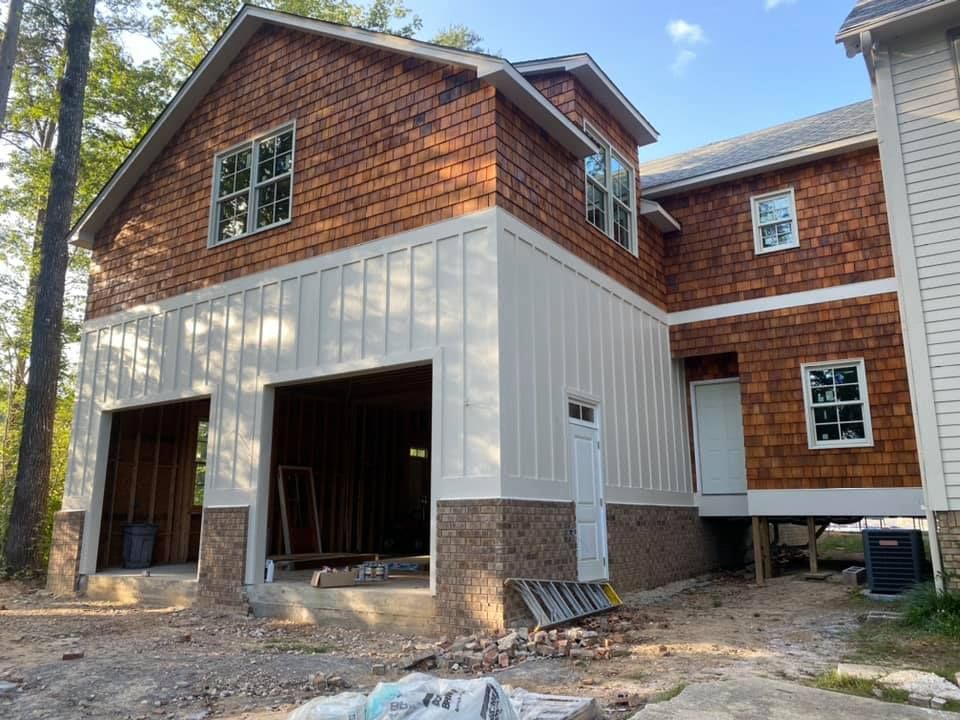 Construction of a two-story building with a garage, featuring cedar shake siding and white paneling.