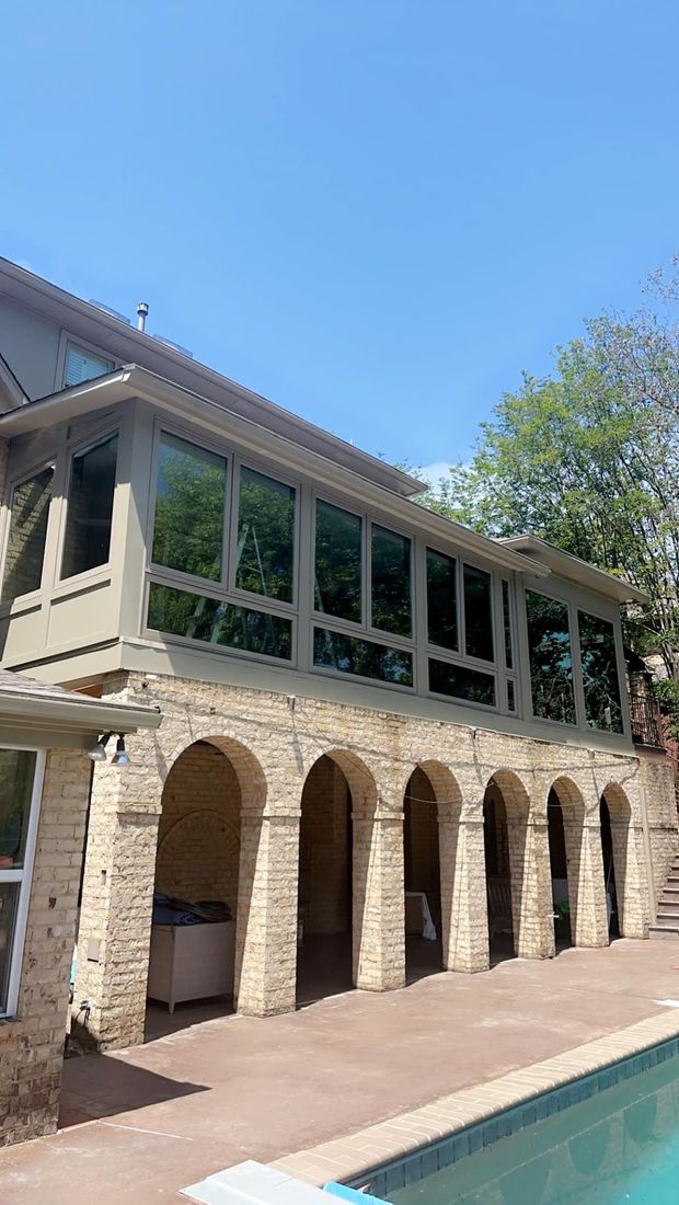 Sunroom with arched columns, large windows, and a pool.