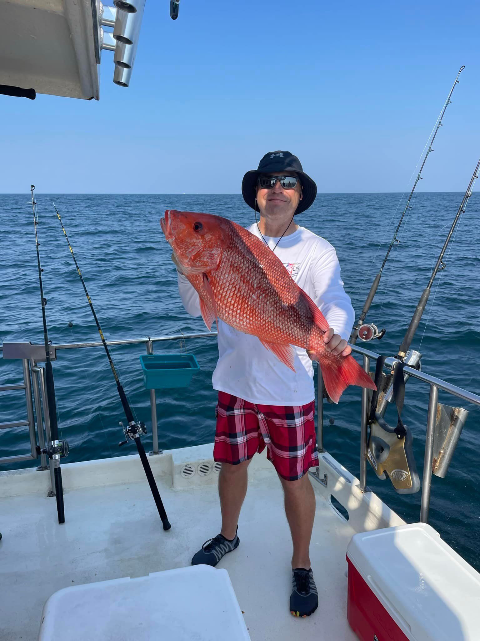 A man is holding a large red fish on a boat.
