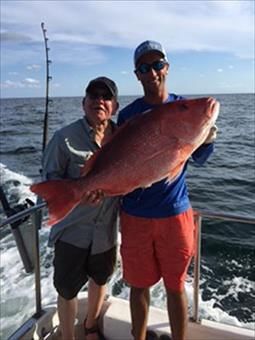 Two men are standing on a boat holding a large red fish.