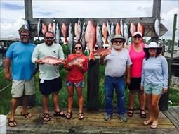 A group of people are standing on a dock holding fish.