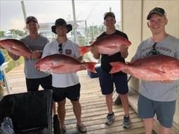 A group of men are standing on a deck holding large fish.