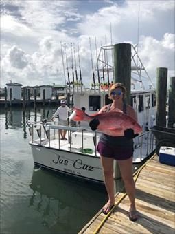 A woman is holding a large fish in front of a boat.