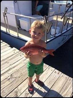 A young boy is holding a fish on a dock.
