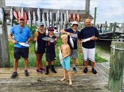 A group of people are standing on a dock holding fish.