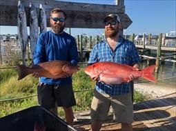 Two men are standing next to each other holding large red fish.