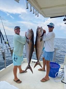 Two men are standing on a boat holding two large fish.