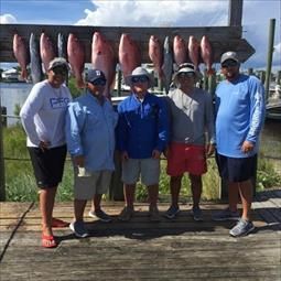 A group of men are standing on a dock with fish hanging from a rack.