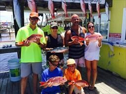 A group of people are standing on a dock holding fish.