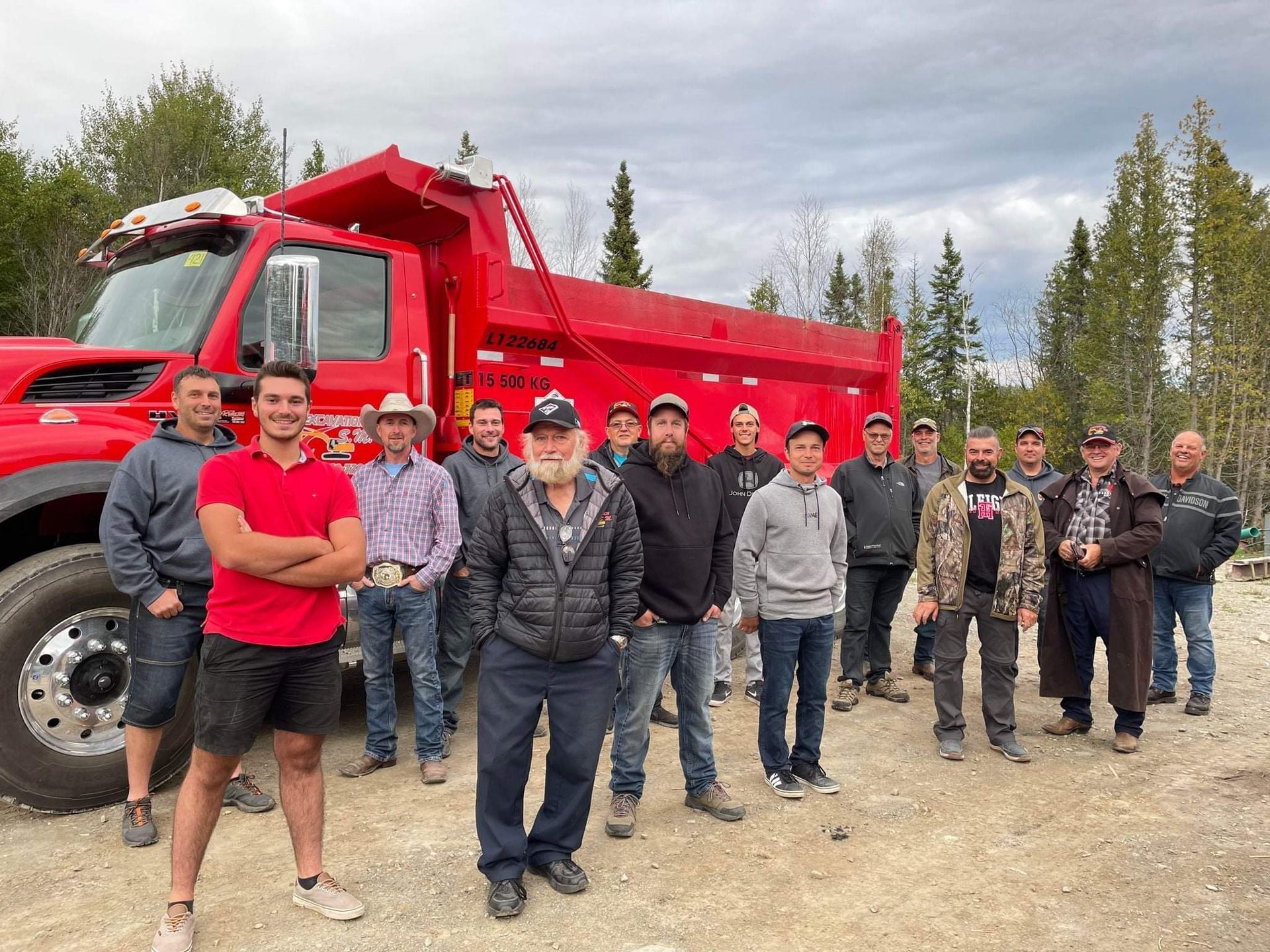 Un groupe d’hommes se tient devant un camion-benne rouge.