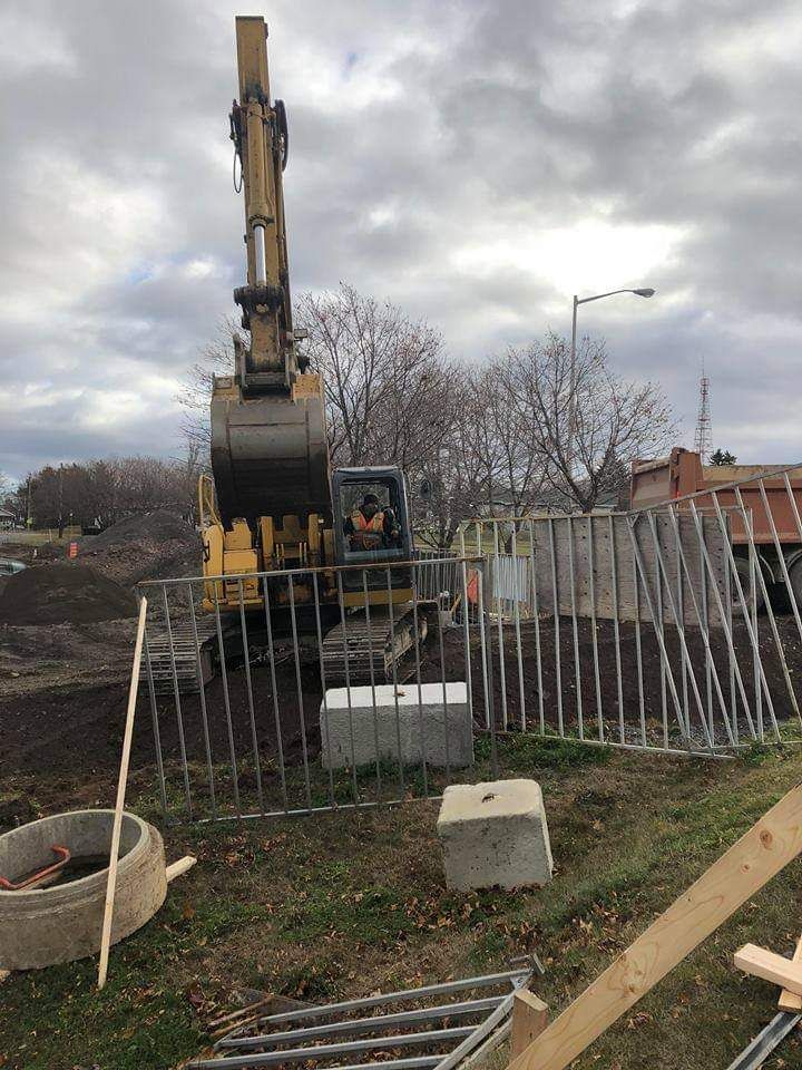 Une excavatrice jaune déplace de la terre sur un chantier de construction derrière une clôture.
