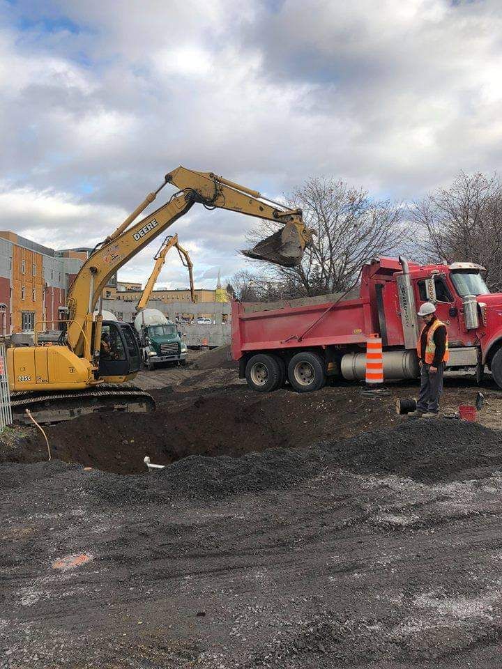 Une excavatrice jaune charge de la terre dans un camion à benne rouge.