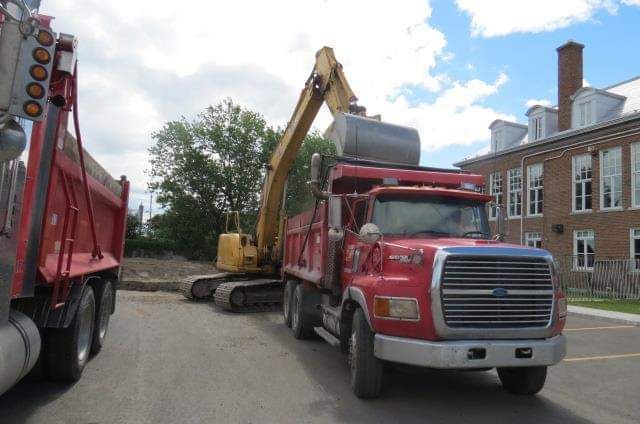 Un camion à benne rouge avec une excavatrice jaune dessus
