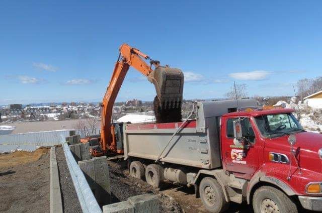Un camion-benne rouge est chargé de terre par une excavatrice.