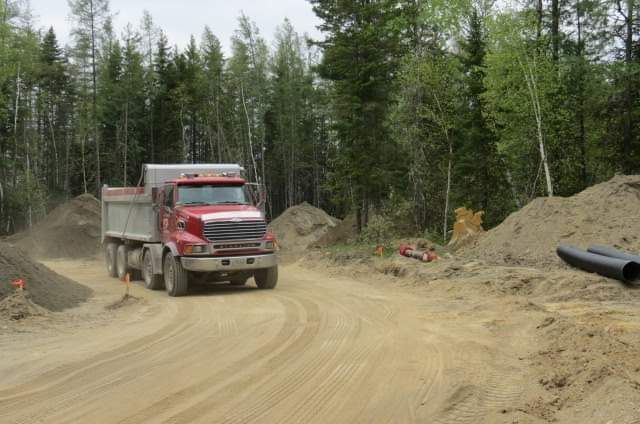 Un camion-benne rouge roule sur un chemin de terre.