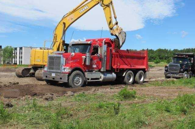 Un camion-benne rouge est chargé de terre par une excavatrice jaune.