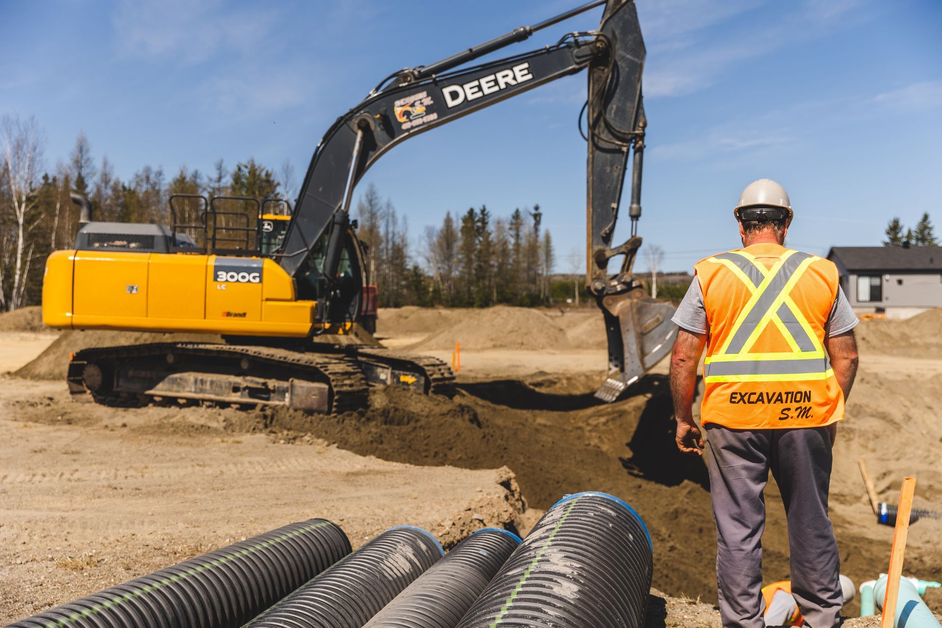 Un ouvrier du bâtiment se tient devant une excavatrice Deere.