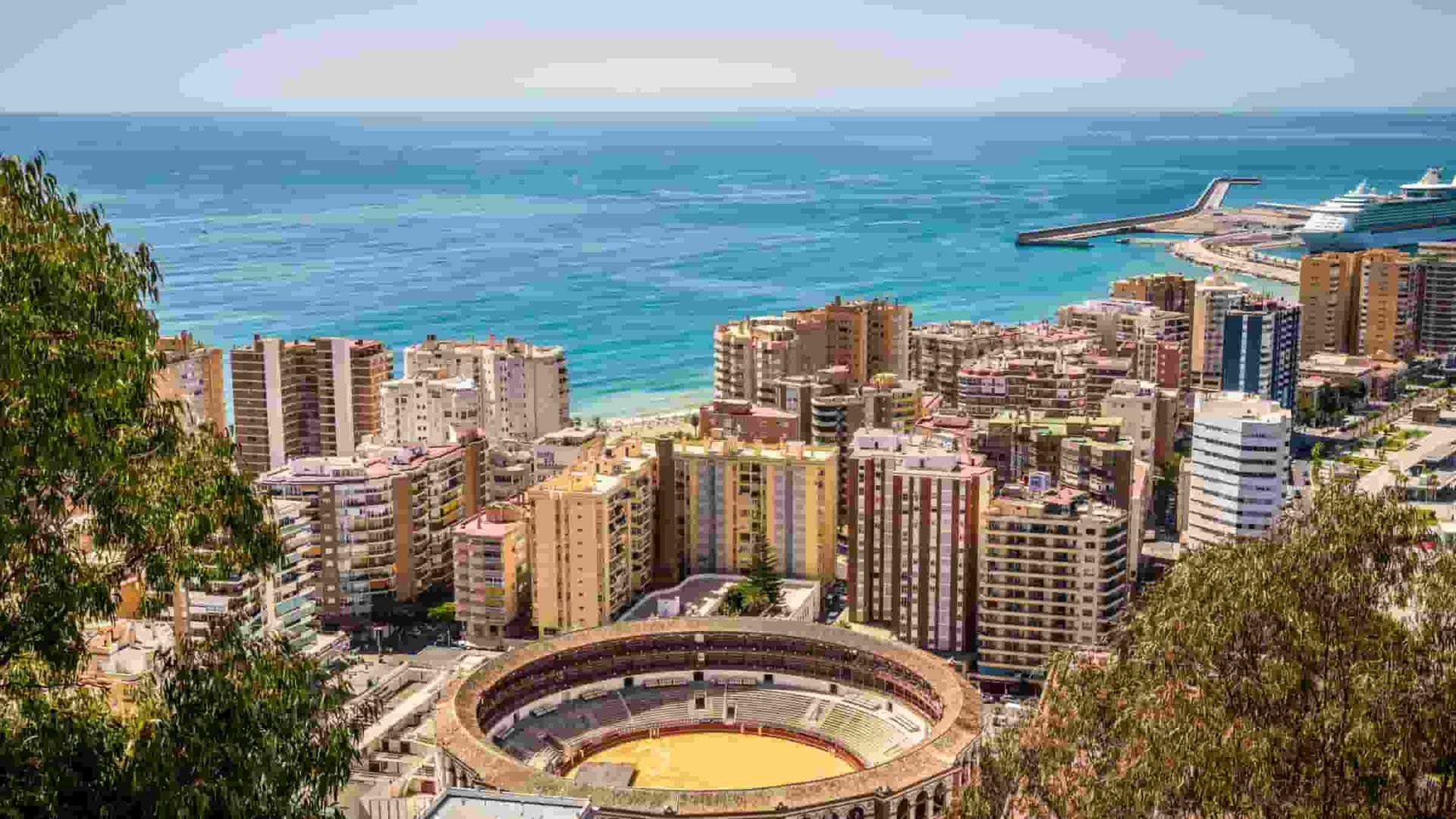 An aerial view of Malaga with a bullring in the foreground and the ocean in the background.