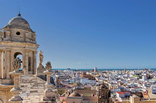 A large building with a dome sits on the shore of a body of water in Cadiz