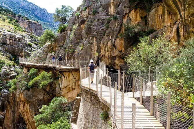 A group of people are walking on a bridge between two cliffs in Caminito del rey