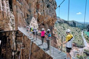 A group of people are standing in Caminito del rey  on a bridge between two cliffs.