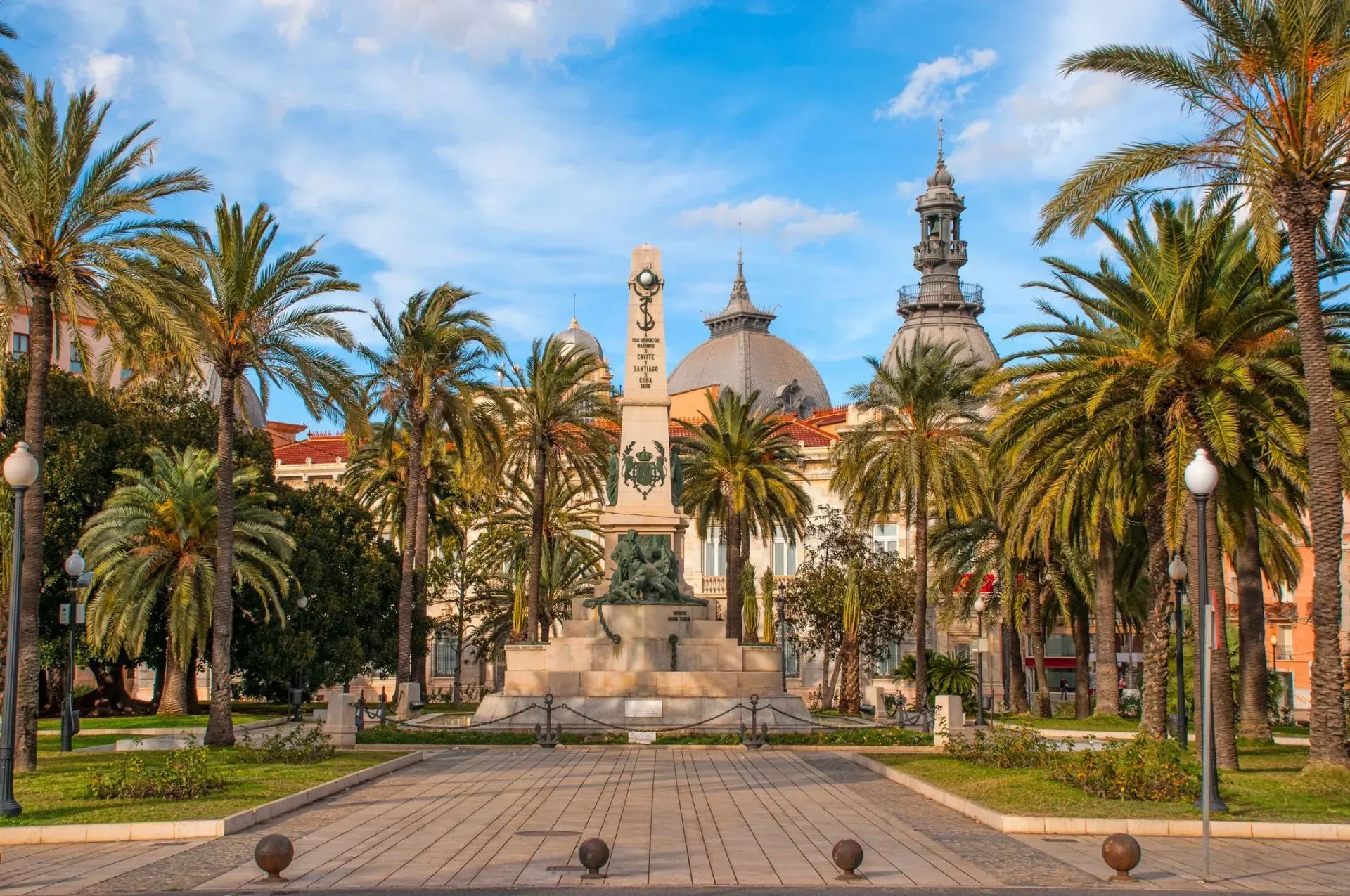 There is a statue in the middle of a park surrounded by palm trees in Cartagena,Spain.