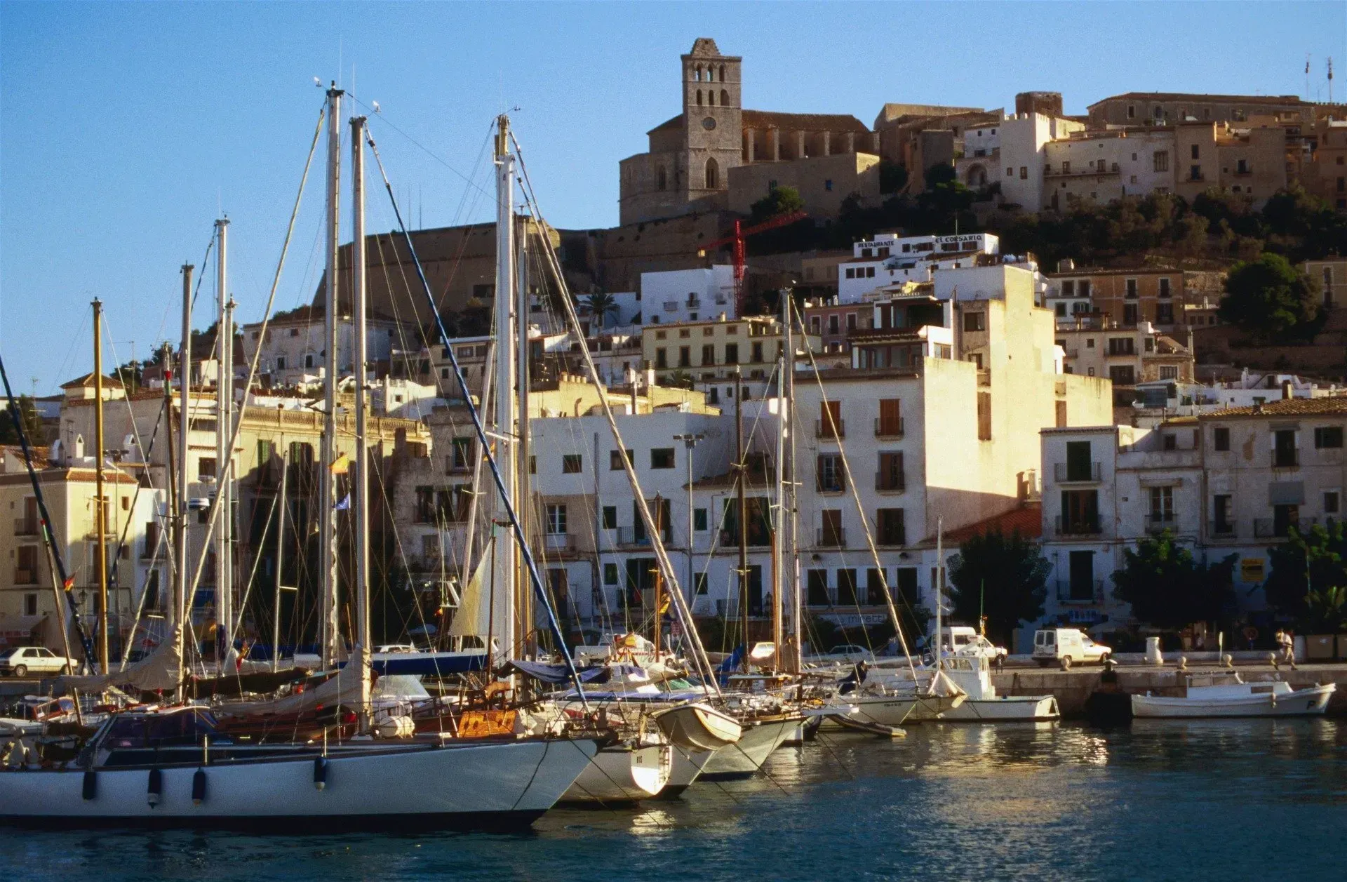 Boats are docked in Ibiza harbor with a city in the background