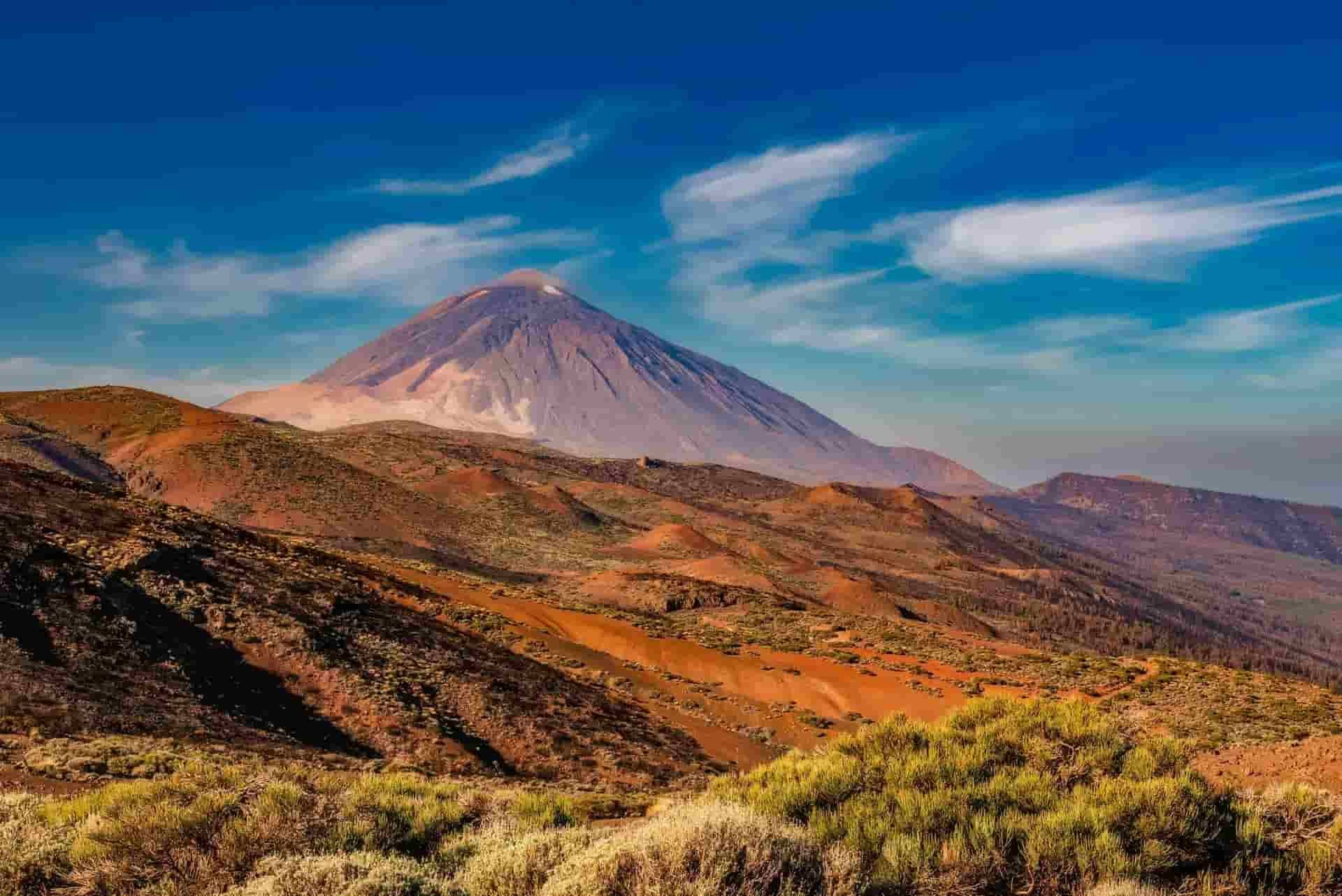 A volcano in Tenerife rises above a desert landscape with mountains in the background.