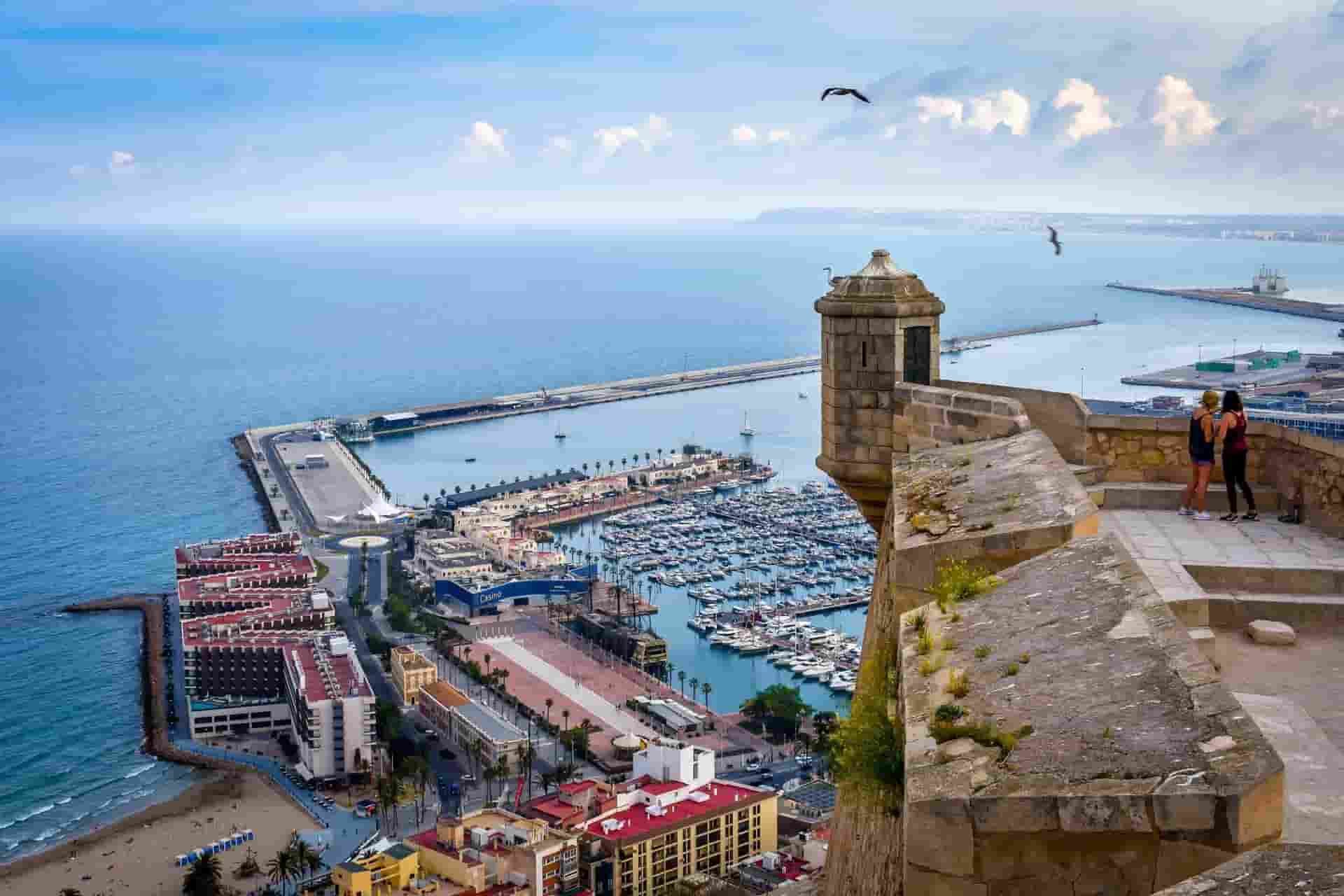 A couple standing on top of a cliff overlooking Alicante and the ocean.