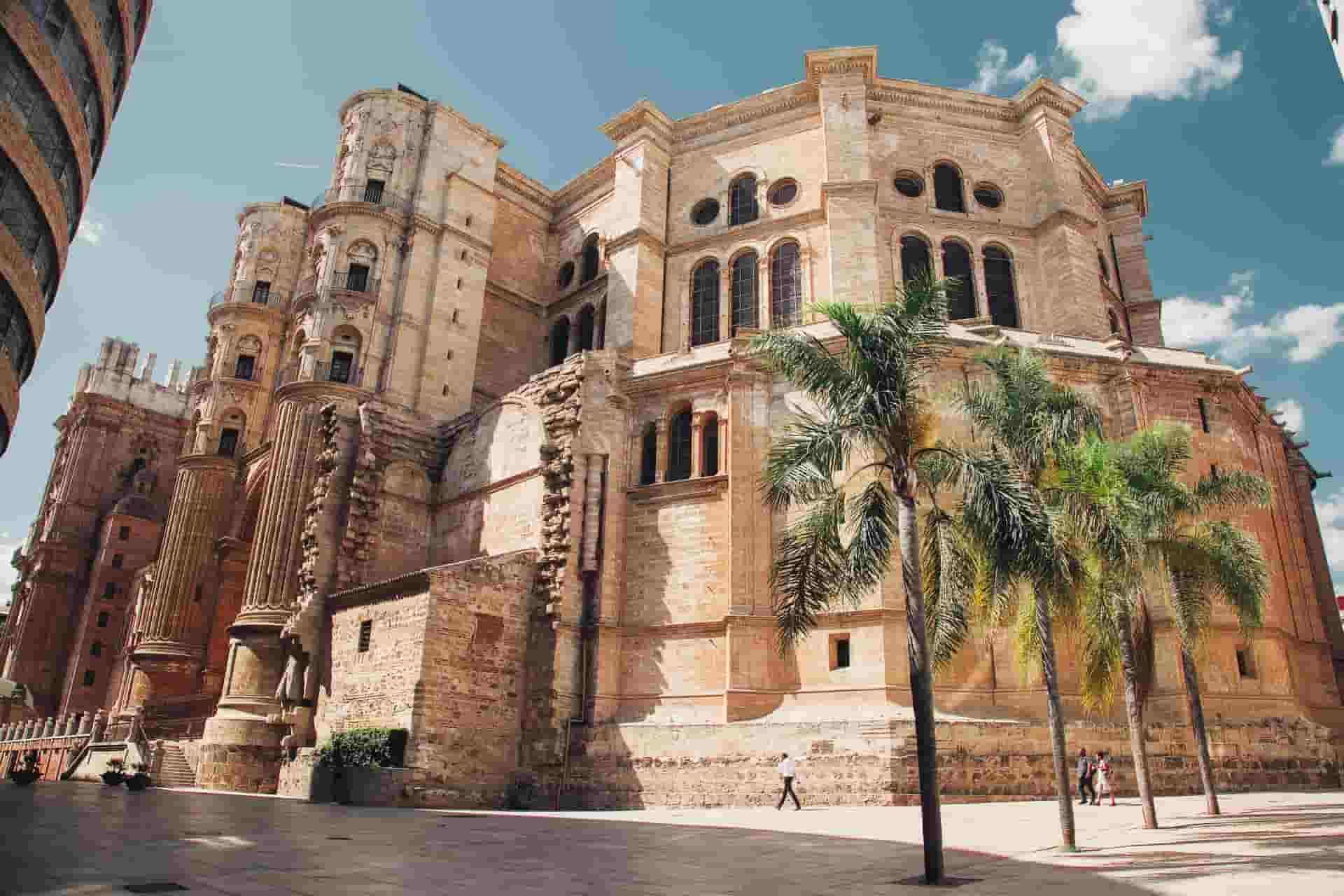 A large Malaga building with a lot of windows and palm trees in front of it.