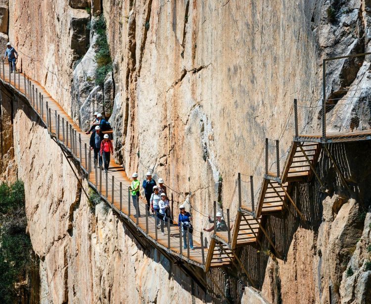 A group of people are walking across a bridge between two cliffs.