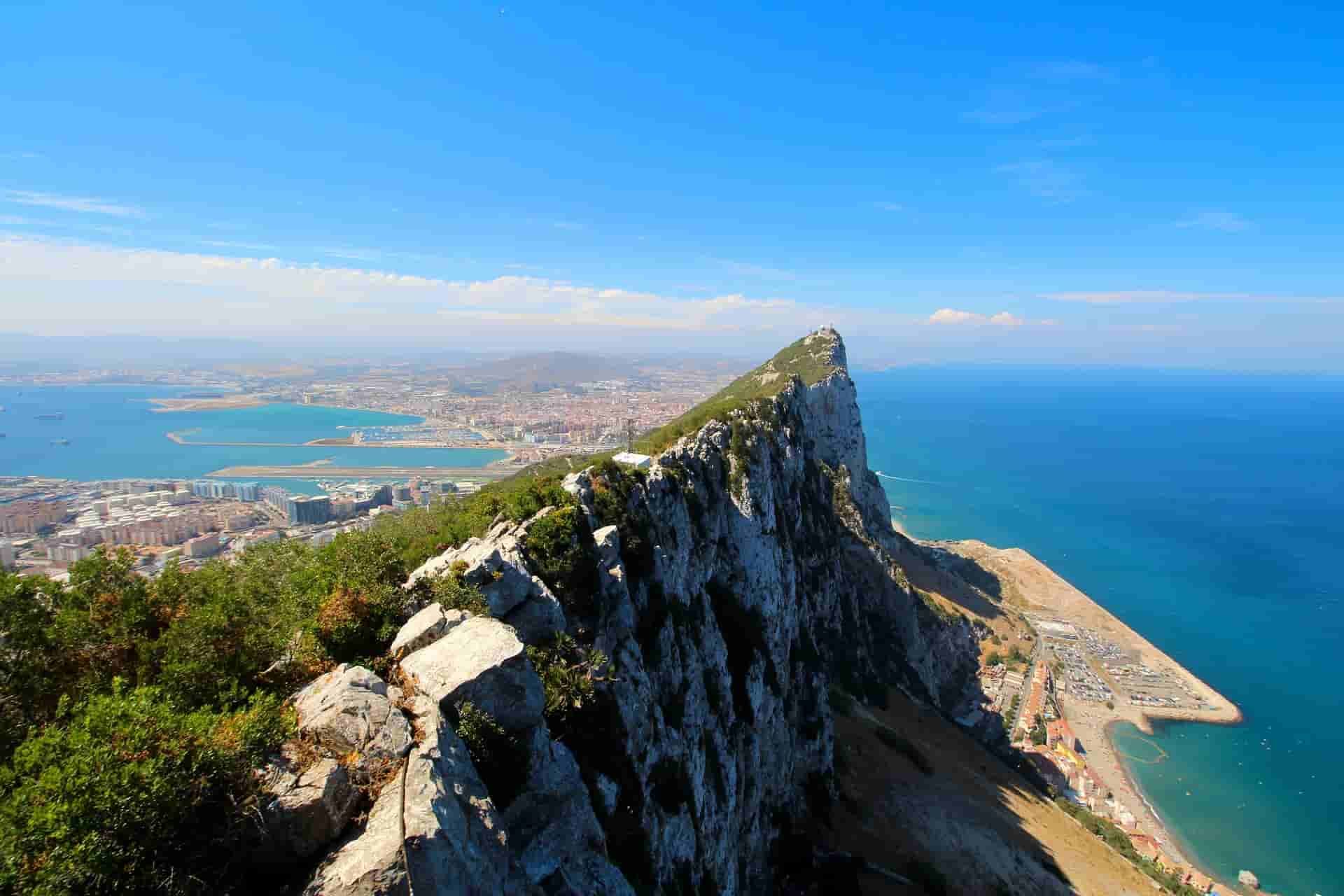 A sailboat is floating in the ocean with Gibraltar  in the background.